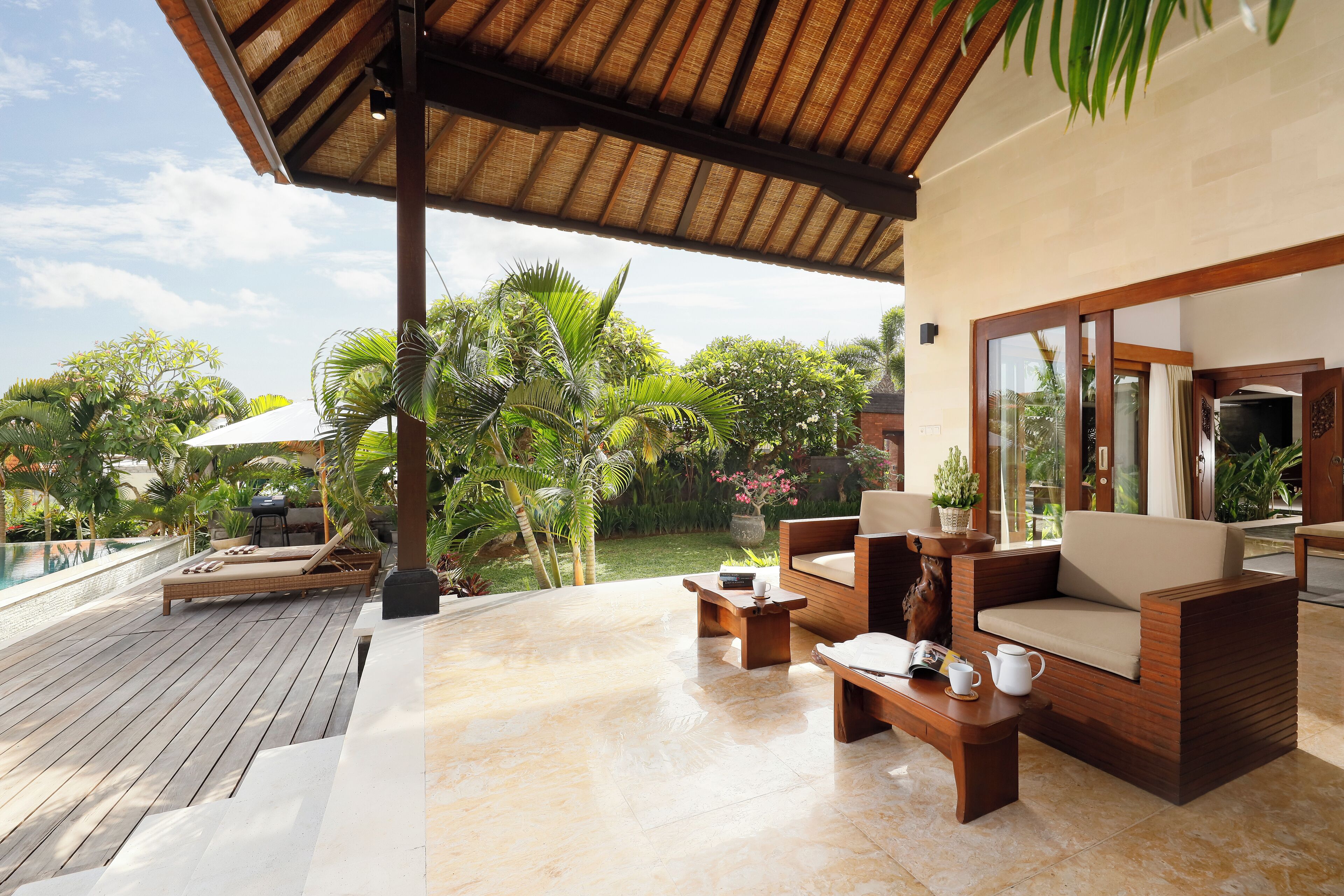A covered outdoor area with a wooden deck, a lounge chair, a sofa, and a coffee table.