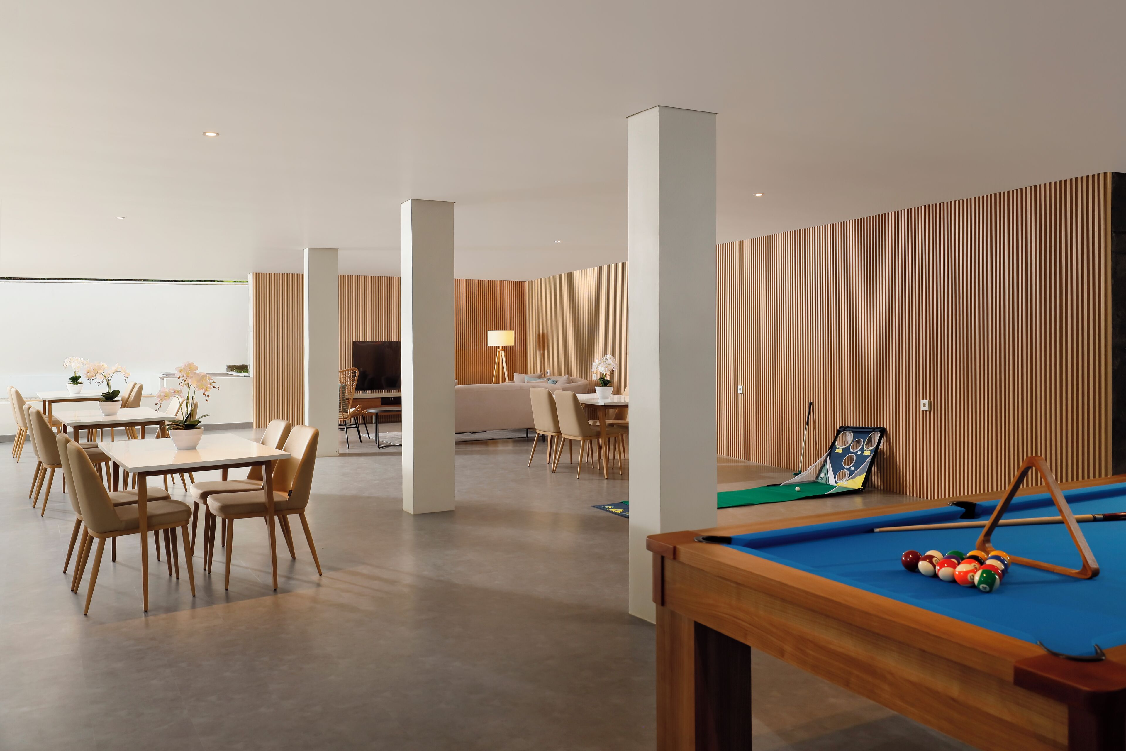 Una habitación de hotel moderna con mesa de billar, zona de comedor y un salón con sofá y sillones.