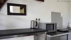 A kitchenette with a microwave, kettle, and a small countertop. There are two chairs and a mirror on the wall. - Hôtel Mas le Sauvageon (Saintes-Maries-de-la-Mer)