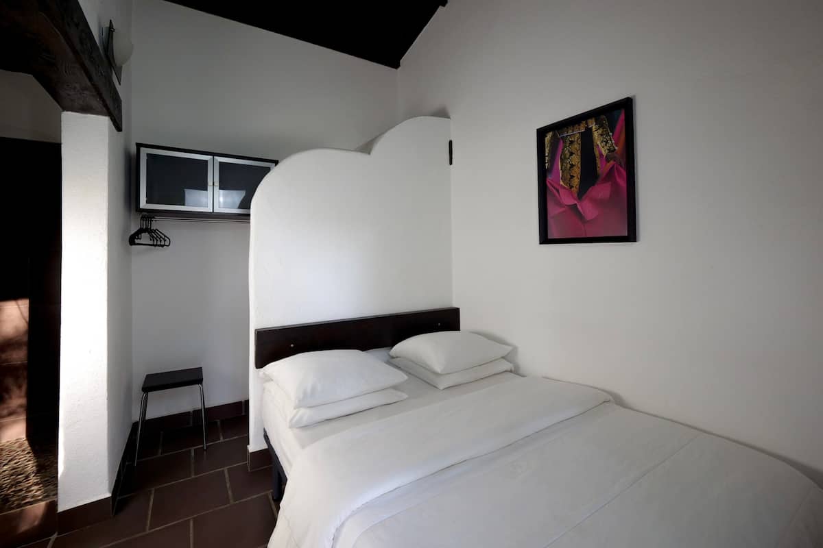 Une chambre à coucher avec un lit, une fenêtre, une lampe fixée au mur et un tableau.