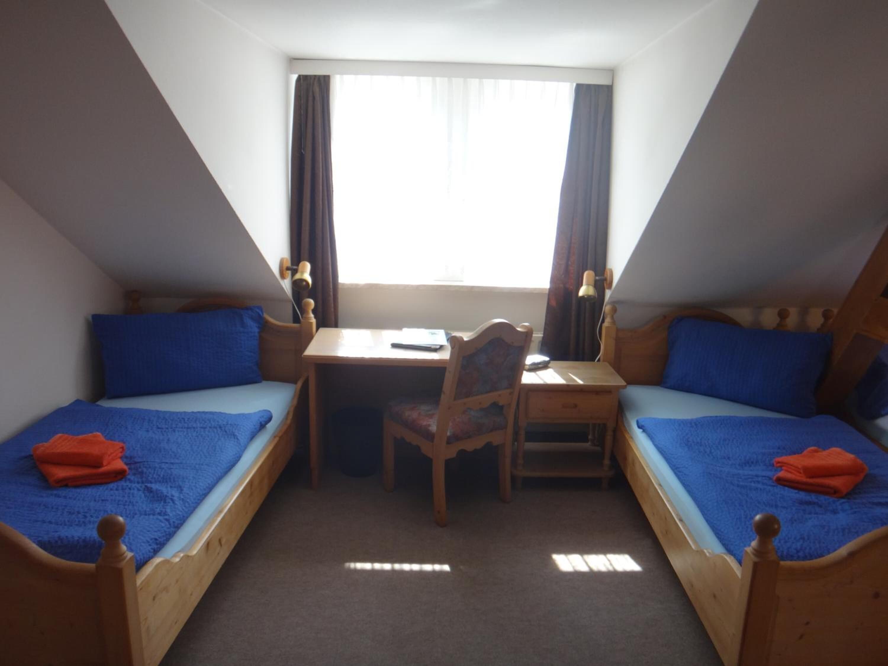 A small, triangular room with two wooden beds, a desk, and a chair.