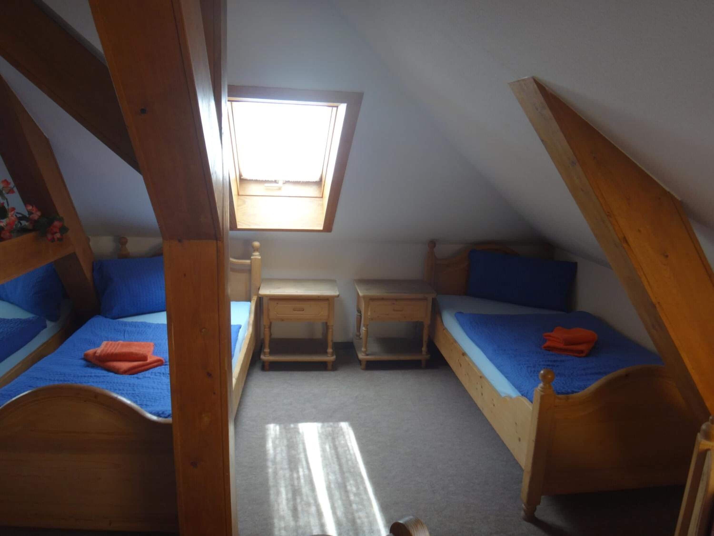 A small attic bedroom with two wooden beds, a small desk, and a window.