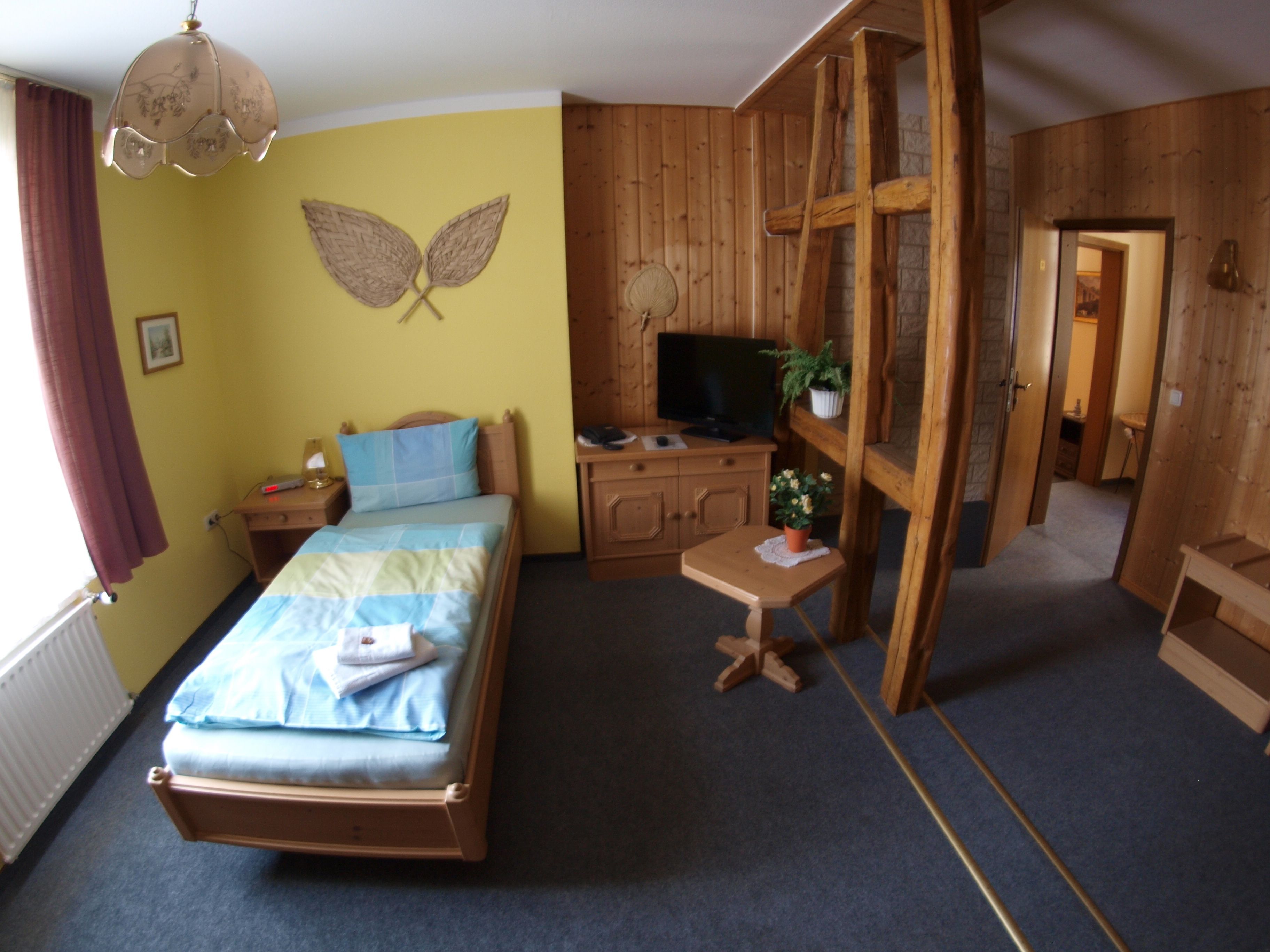 A bedroom with a bed, a desk, a television, and a wooden wardrobe.