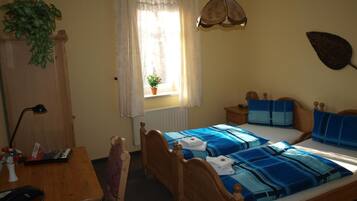A bedroom with a wooden bed, a desk, a chair, a lamp, a window with curtains, and a hanging plant.