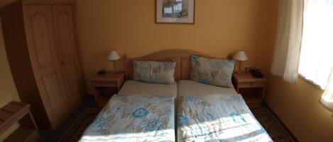A double bed with floral bedding, two bedside tables with lamps, a wardrobe, and a framed picture on the wall.