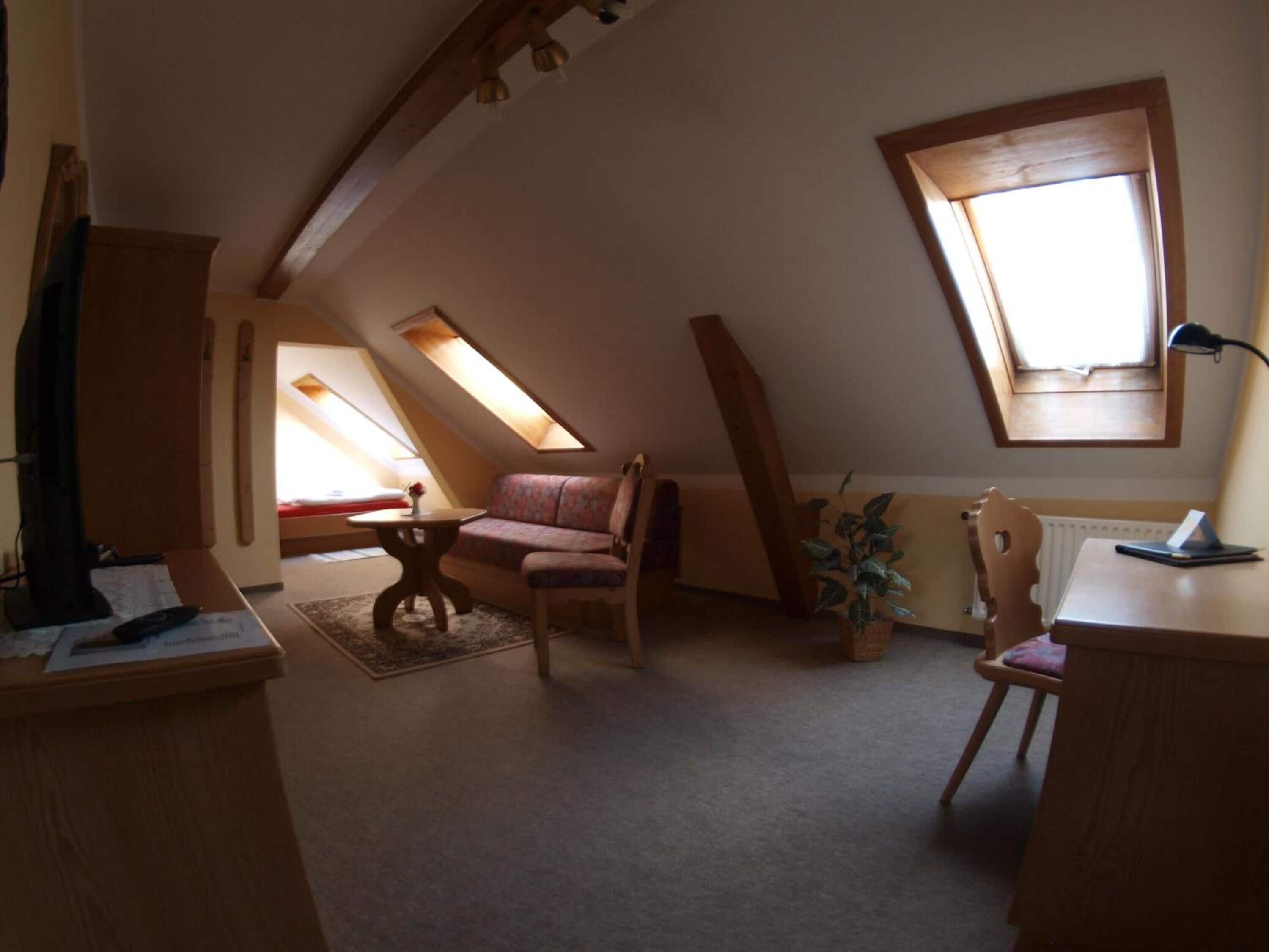 A cozy attic room with a sloped ceiling, a sofa, a chair, a small table, and a potted plant.