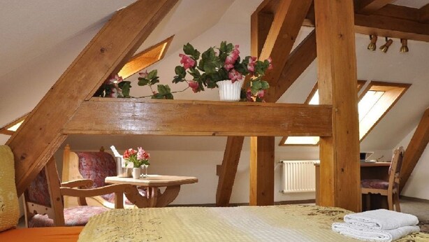 Un dormitorio acogedor en el ático, con techo de madera, una cama, una mesita y una silla.