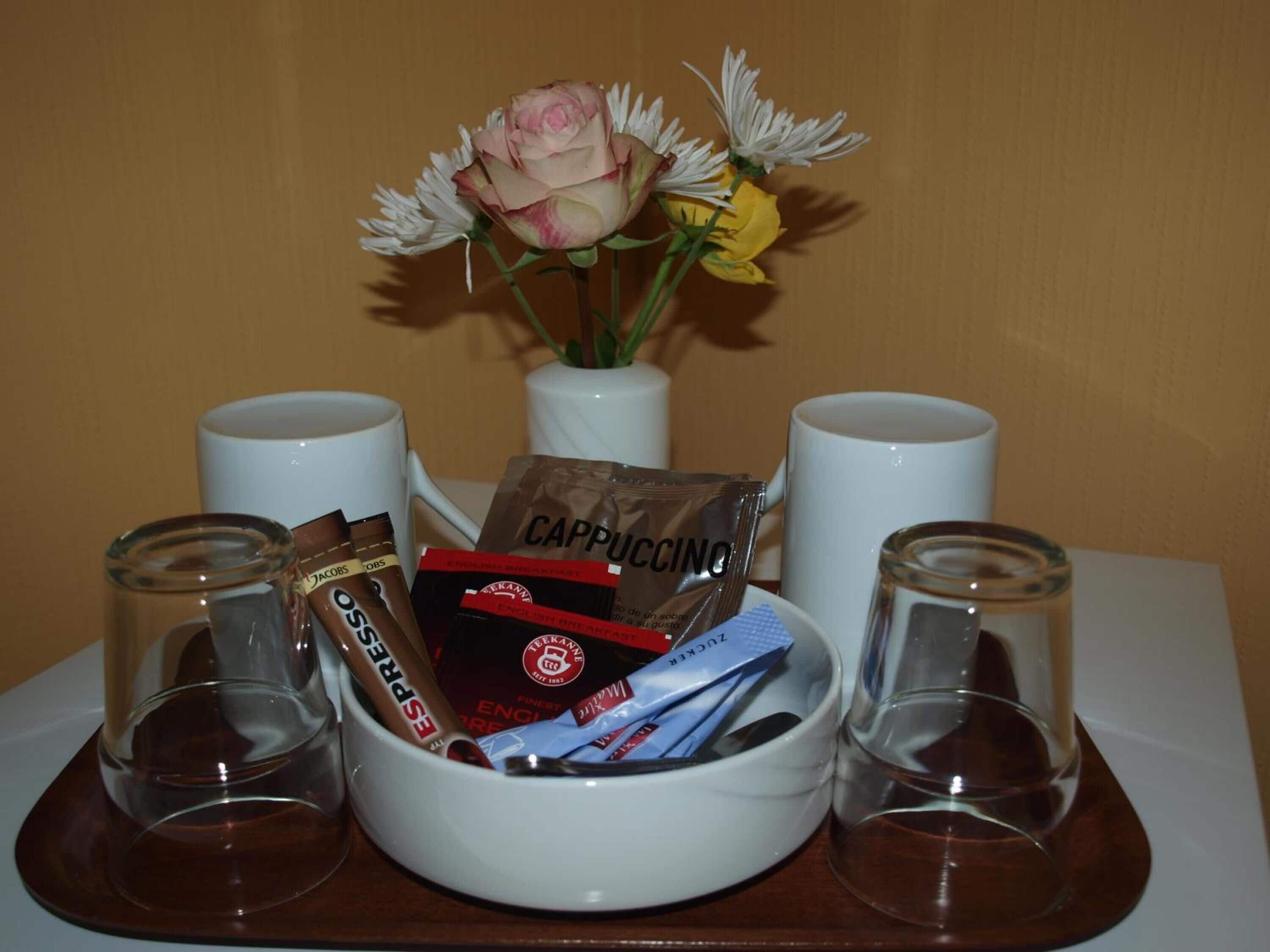 Et bord med en hvid skål med kaffeposer, en vase med blomster og to tomme glas.