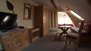Un dormitorio acogedor en el ático con un aparador de madera, un televisor, una mesita con una silla y un ventanal grande que proporciona luz natural.