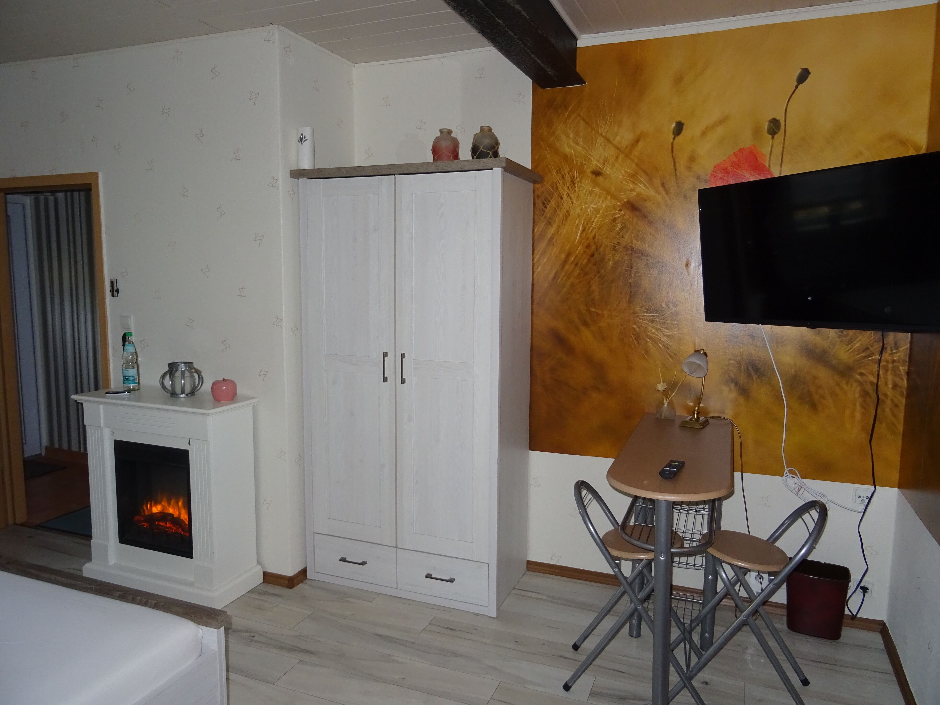 Una habitación con chimenea, un armario blanco, una mesa de comedor con sillas y un televisor montado en la pared.