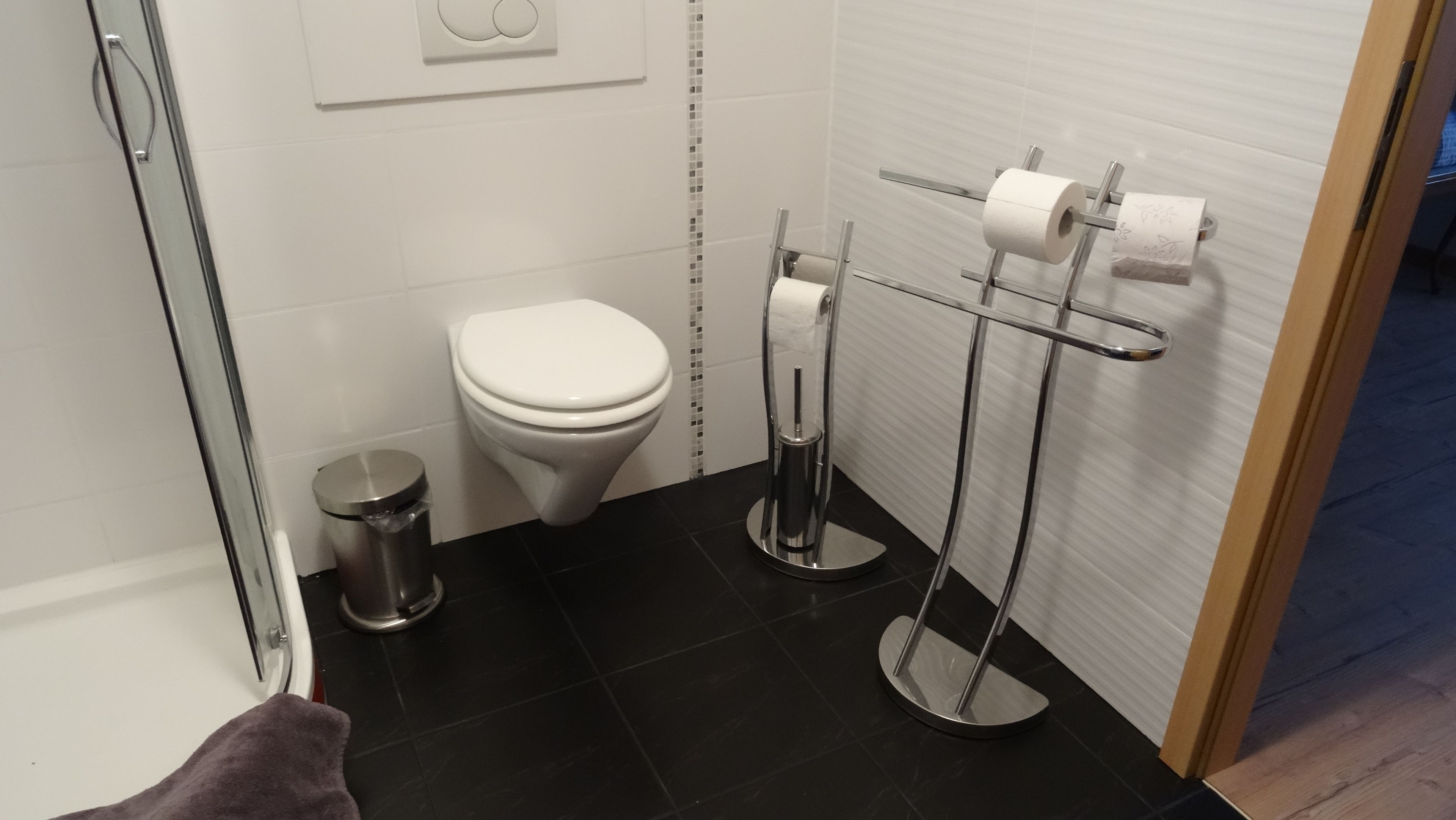 Egy modern fürőszoba, amelyben található egy WC, egy szemeteskosár és egy WC-papírtartó.
