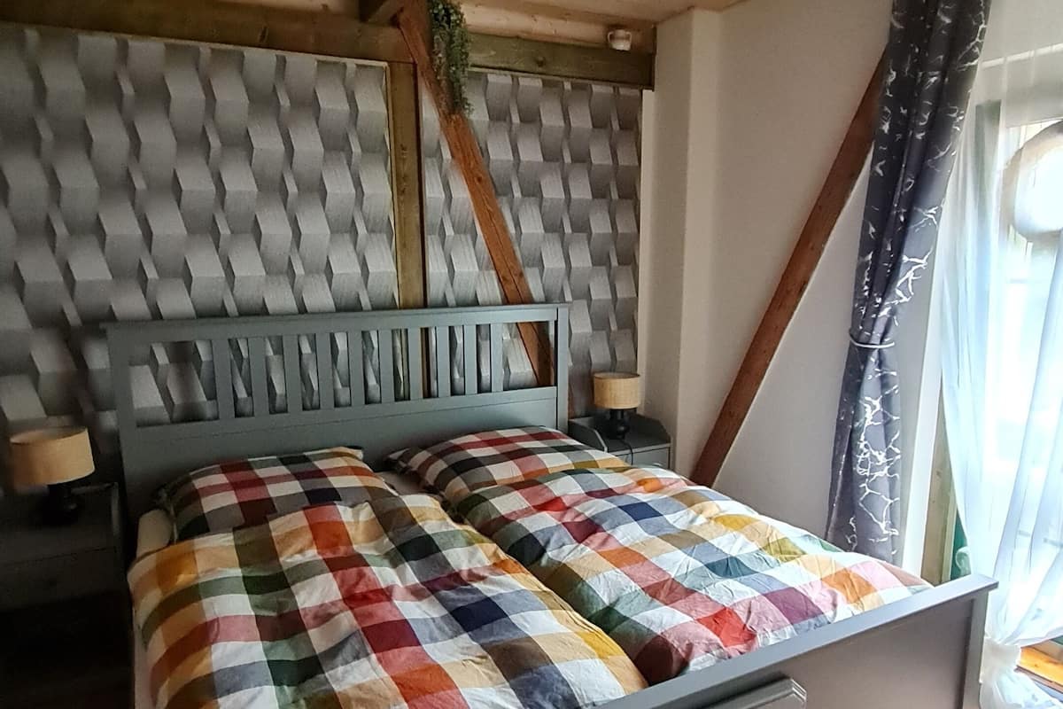 Une chambre à coucher comprenant un lit, une table de chevet, une commode, une tête de lit et une fenêtre avec des rideaux.