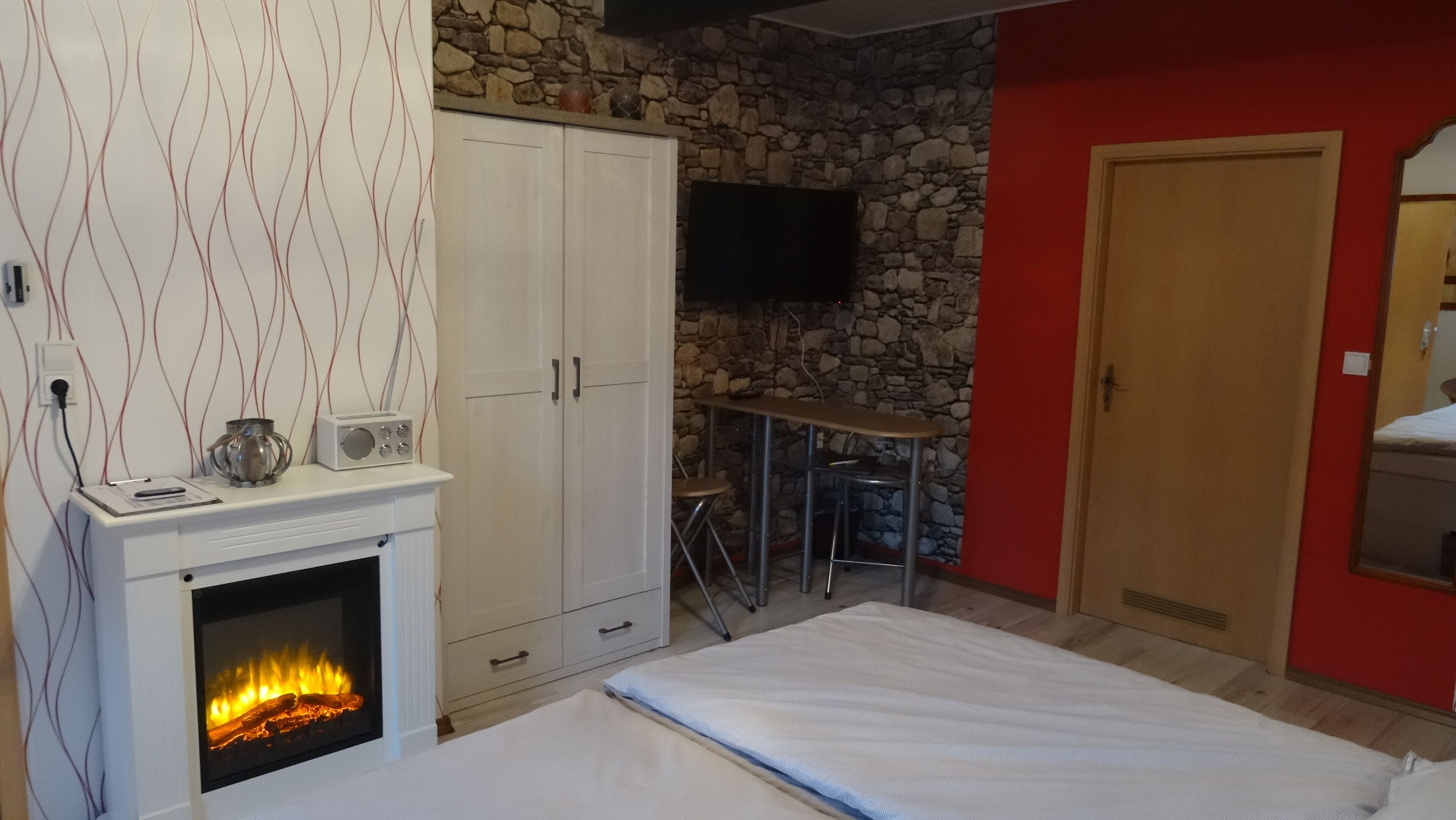 Ein Schlafzimmer mit Kamin, einem an einer Steinwand montierten Fernseher, einem kleinen Tisch mit Stühlen und einem Bett.