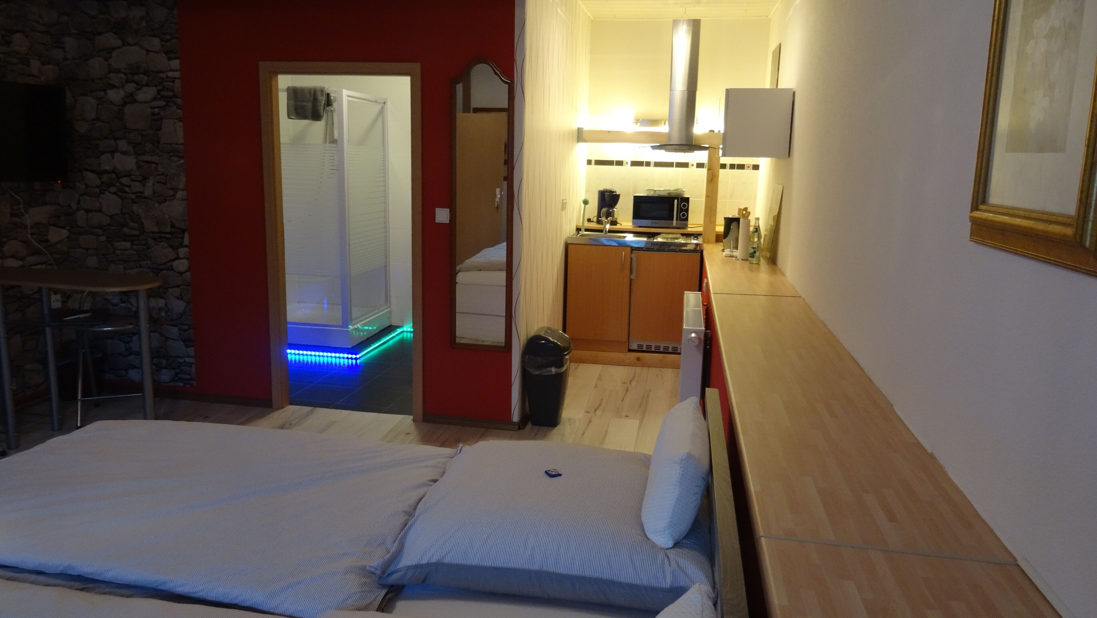 A hotel room with a bed, a small kitchenette, a bathroom with a shower, and a dining area with a table and chairs.