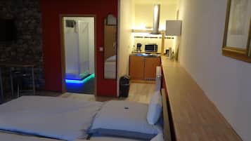 A hotel room with a bed, a small kitchenette, a bathroom with a shower, and a dining area with a table and chairs.