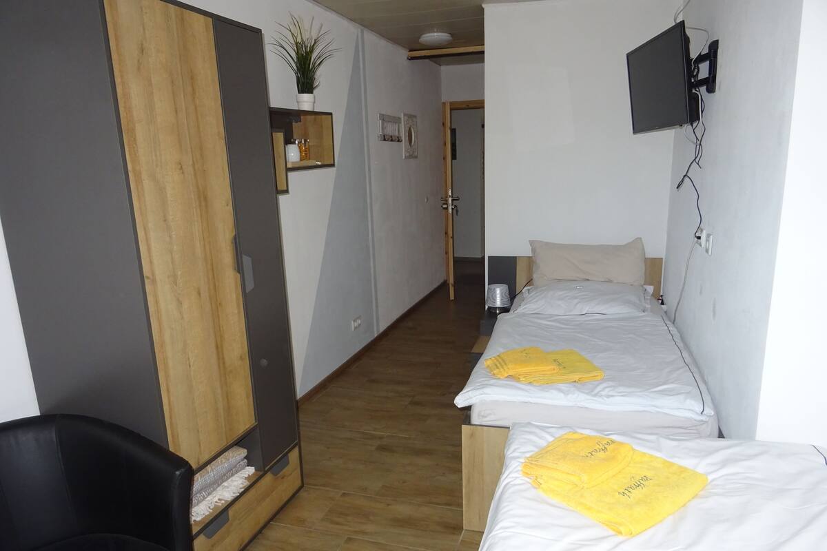Une chambre d’hôtel avec deux lits, une armoire en bois, un petit bureau, une chaise et un téléviseur fixé au mur.