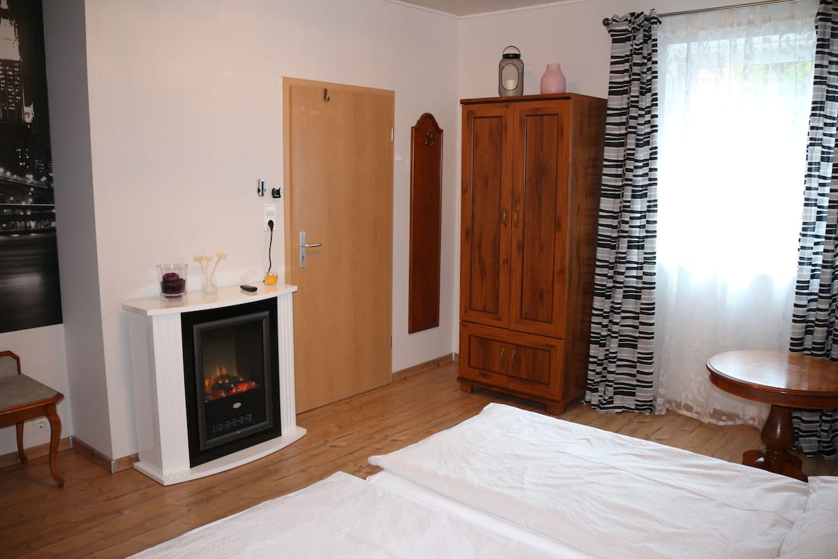 Une pièce avec une cheminée, une armoire en bois, une table ronde et un lit.