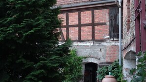 Ein historisches Gebäude mit Ziegelverkleidung und einem großen Baum im Vordergrund.