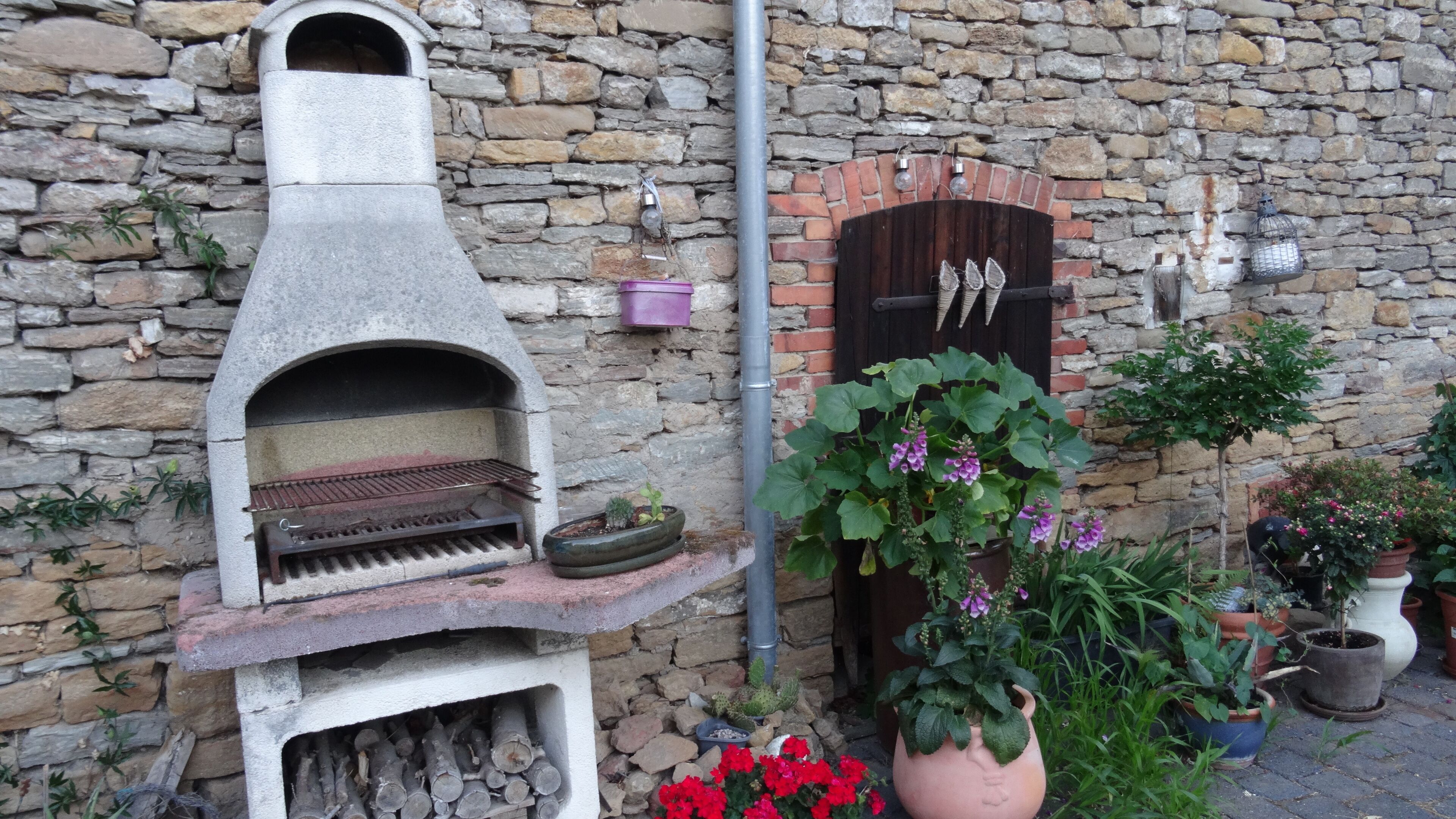A stone wall with a brick oven, a wooden door, and various potted plants.