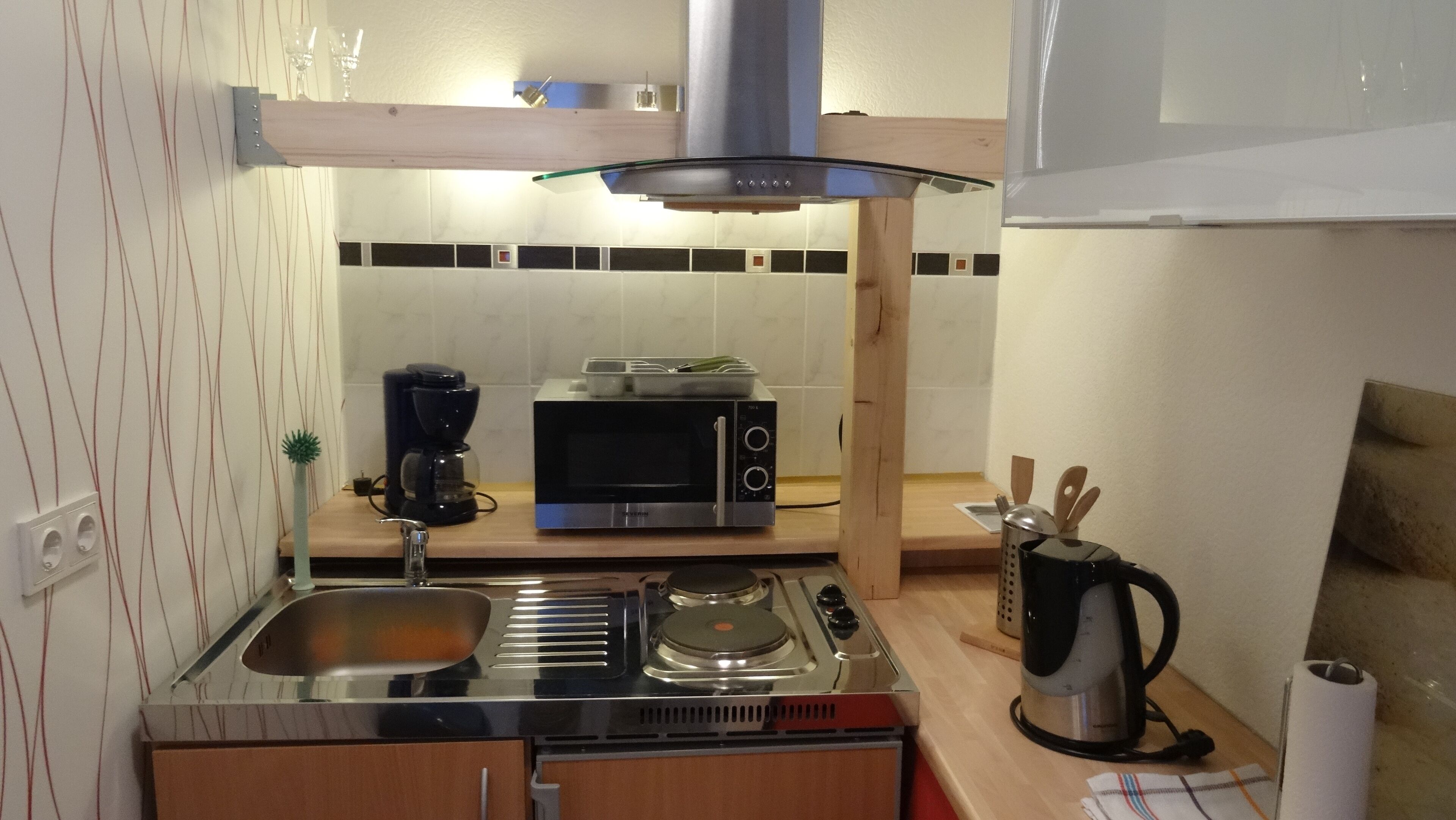 Ett kompakt kök med en gasspis, en mikrovågsugn, en kaffebryggare och en vattenkokare.