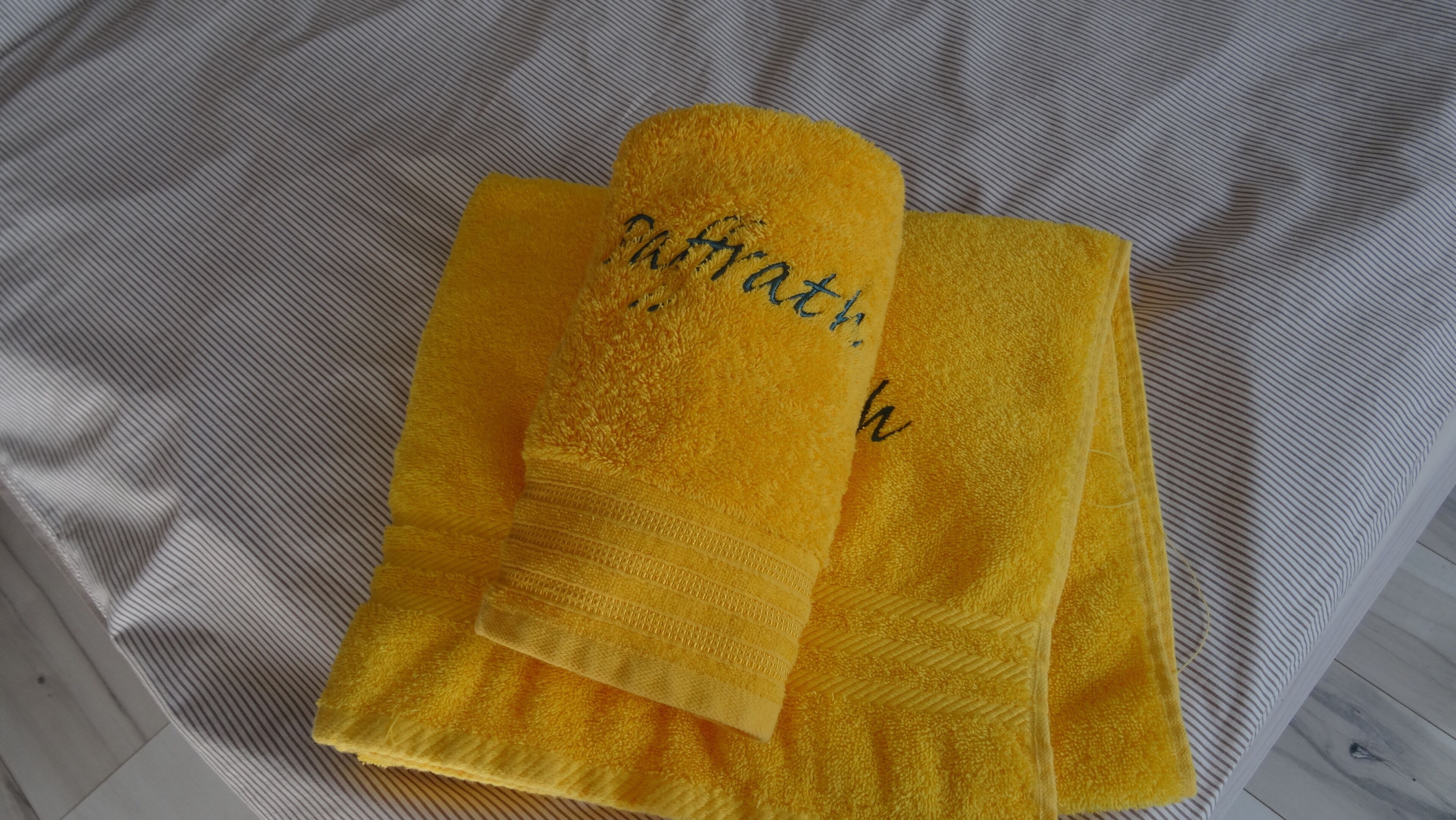 Two yellow towels with embroidered text on a striped fabric background.