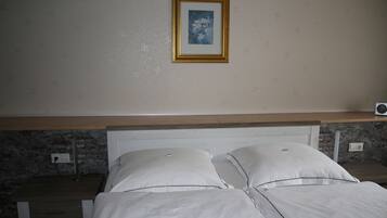 A bedroom with a bed, a nightstand, a wall-mounted picture, and a stone wall.