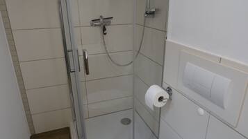 A small, enclosed shower stall with a glass door, a toilet paper holder, and a wall-mounted light switch.