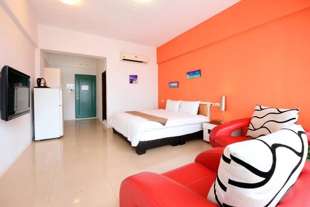 Habitació d'hotel amb un llit, un sofà vermell, una televisió i un aire condicionat.