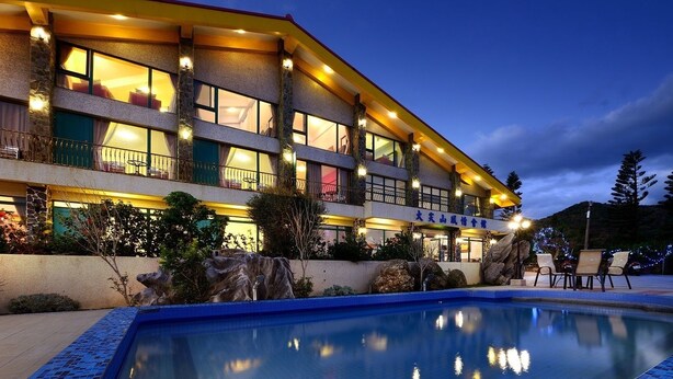 A multi-story hotel with a swimming pool, outdoor seating, and a well-lit facade. - Da Jen Shan Style Resort (Hengchun)