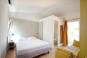 Une chambre à coucher avec un lit, une table de chevet, une chaise et une salle de bain visible à travers une porte ouverte.