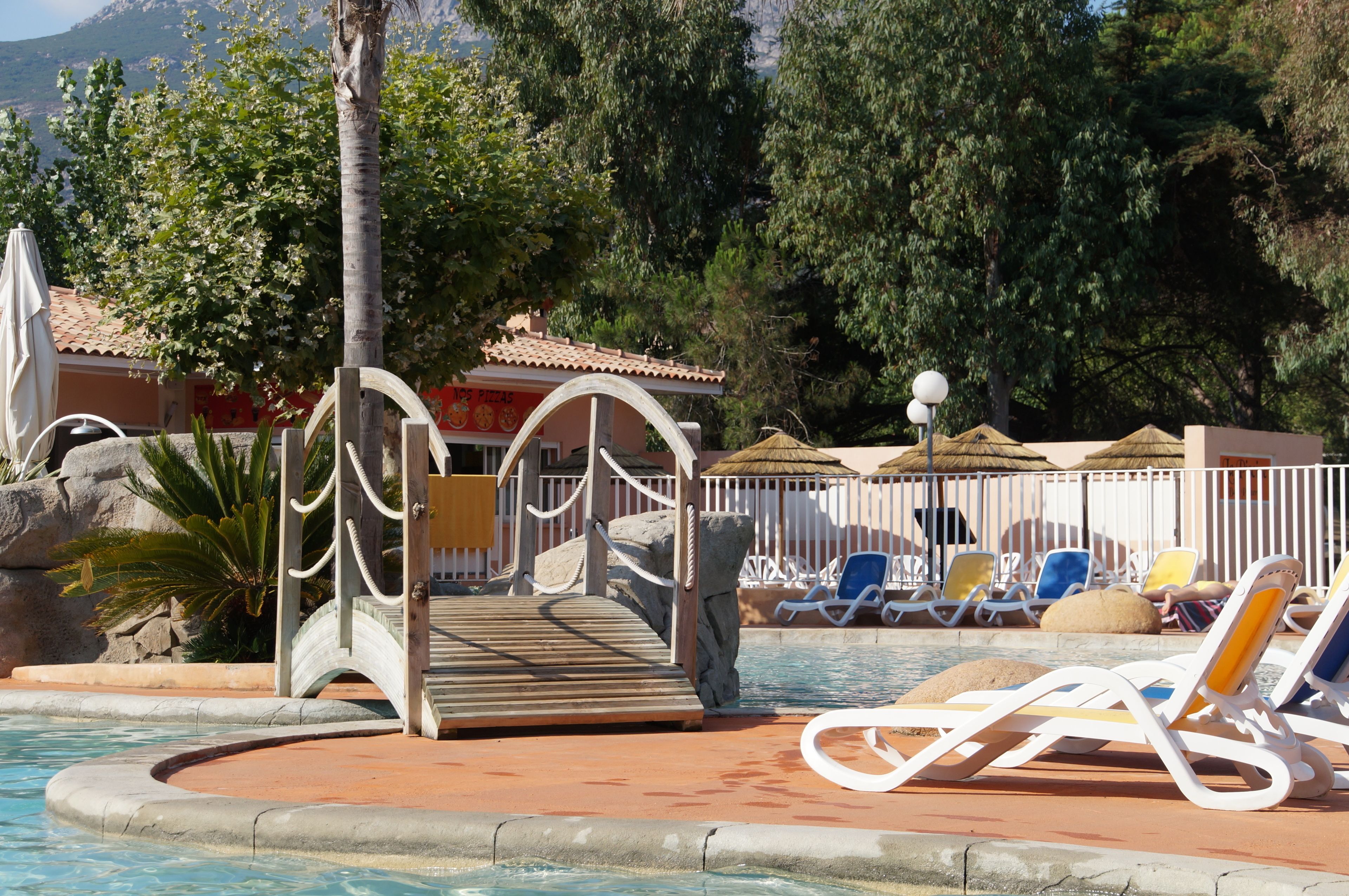 Un área de piscina con sillas de descanso, un puente de madera y una pared de piedra.