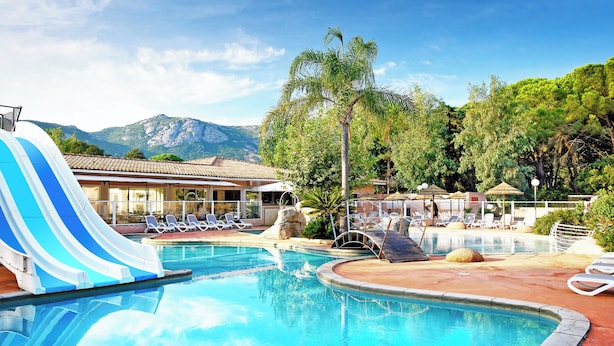 A swimming pool with a blue and white water slide, lounge chairs, and a view of mountains. - Residence Les Castors (Calvi)