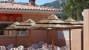 A restaurant with outdoor seating, thatched umbrellas, and a sign advertising pizzas. - Residence Les Castors (Calvi)