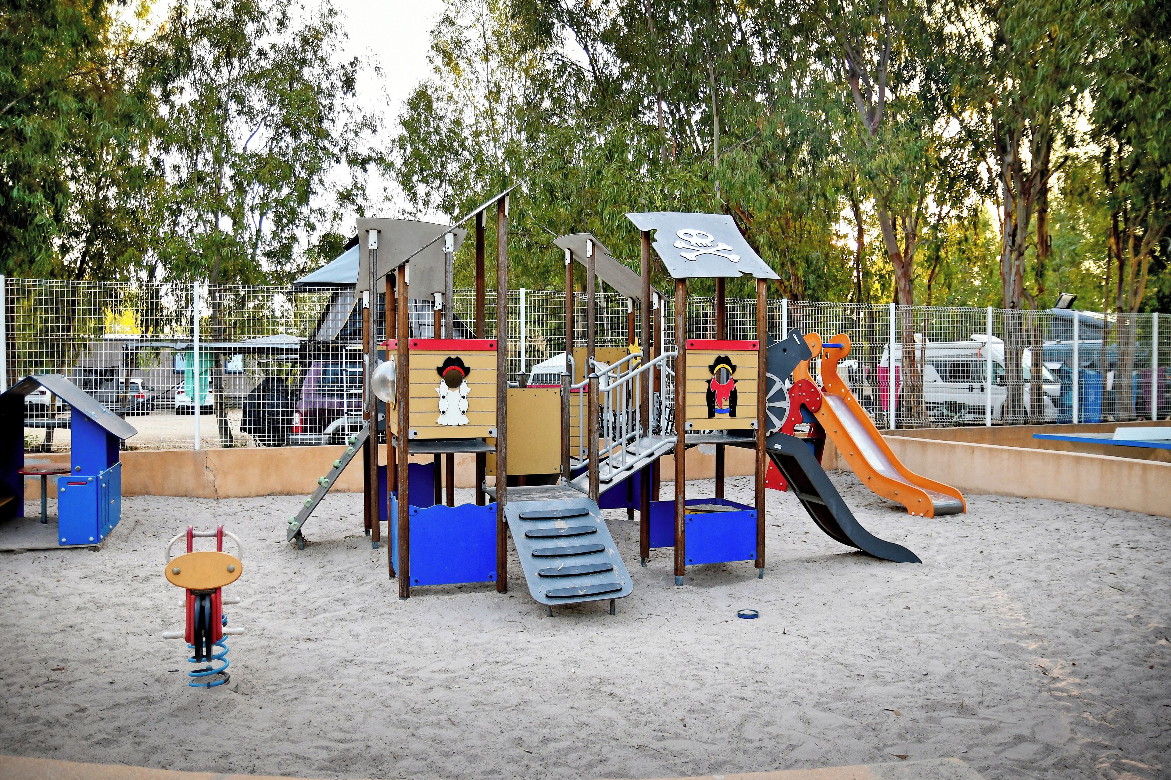 A playground with various play structures, including slides and climbing areas, surrounded by a fenced area.