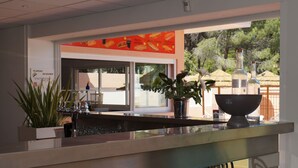 A modern bar area with a glass counter, potted plants, and a menu board. - Residence Les Castors (Calvi)