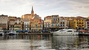 A waterfront with a large yacht docked, buildings with balconies, and a church with a tall steeple. - Residence Les Castors (Calvi)