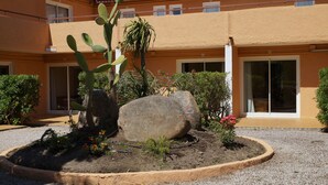 A courtyard with a cactus, a large rock, and a small garden bed with flowers. - Residence Les Castors (Calvi)