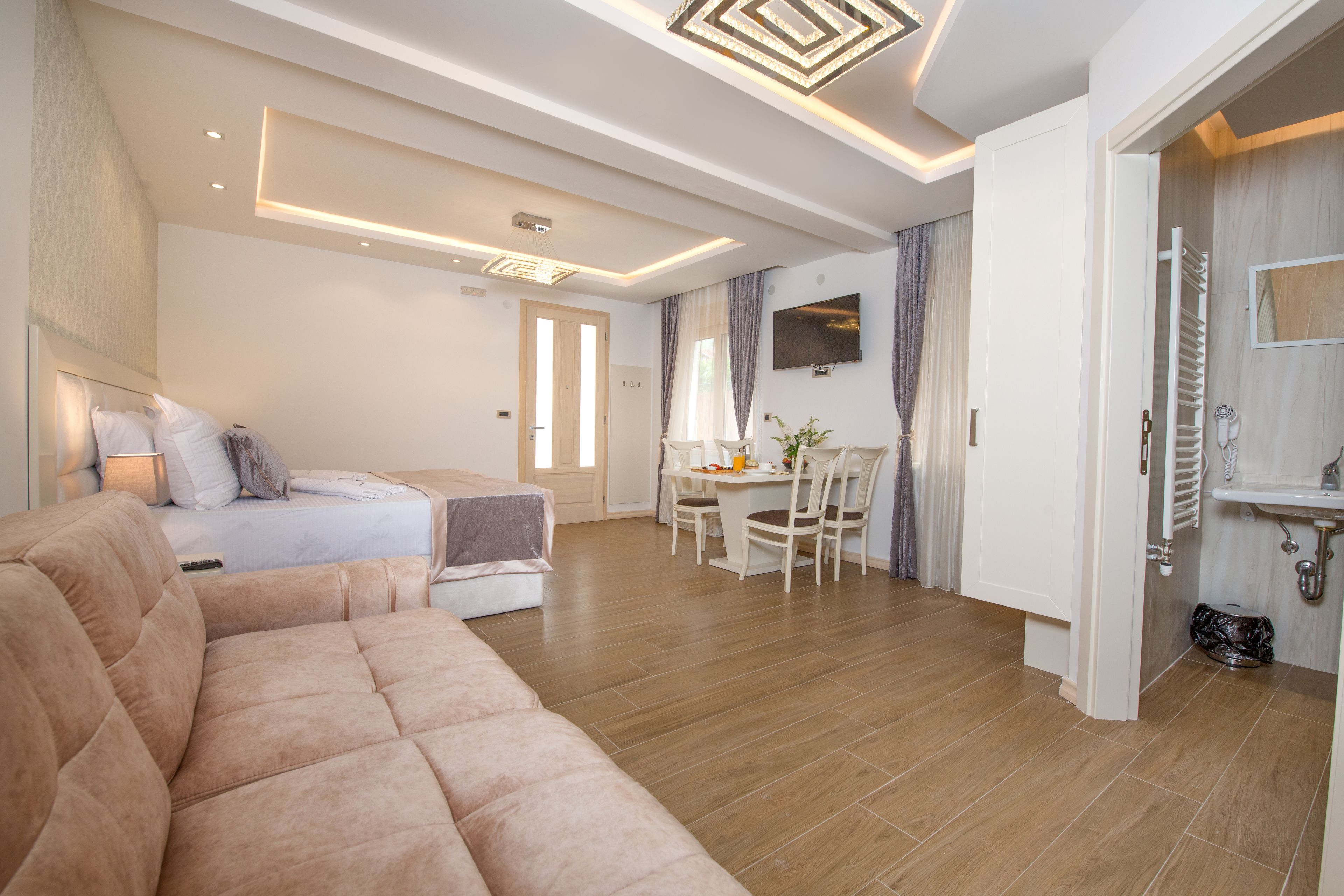 A modern hotel room with a large bed, a sofa, a dining area, and a bathroom.