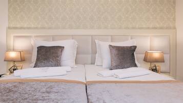 Una cama doble con ropa de cama blanca y marrón, dos lámparas de noche y una pared estampada.