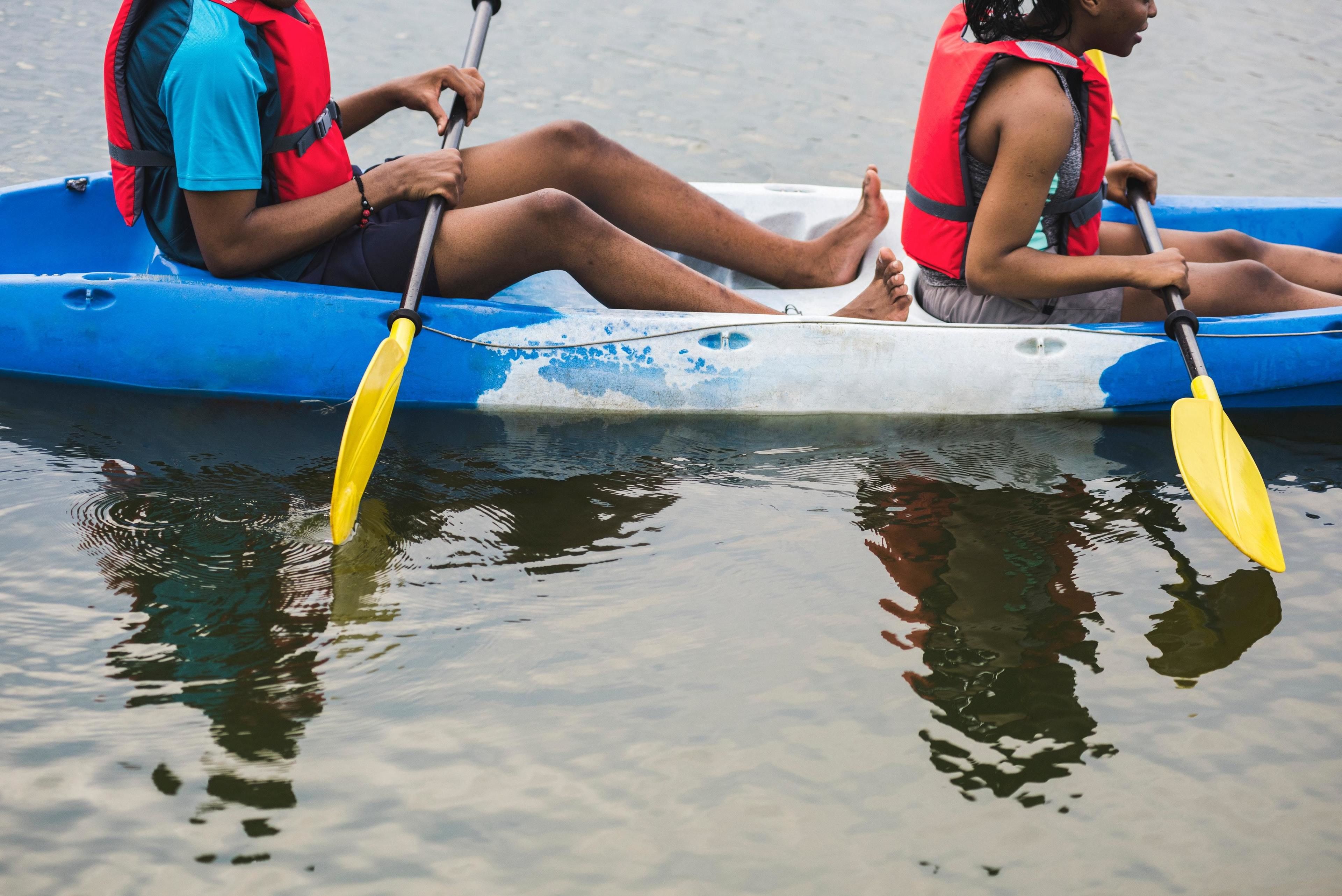 Dos personas en una canoa azul con remos amarillos, vestidas con chalecos salvavidas rojos.