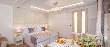Una habitación de hotel moderna con cama, mesita de noche y zona de comedor con mesa preparada para el desayuno.