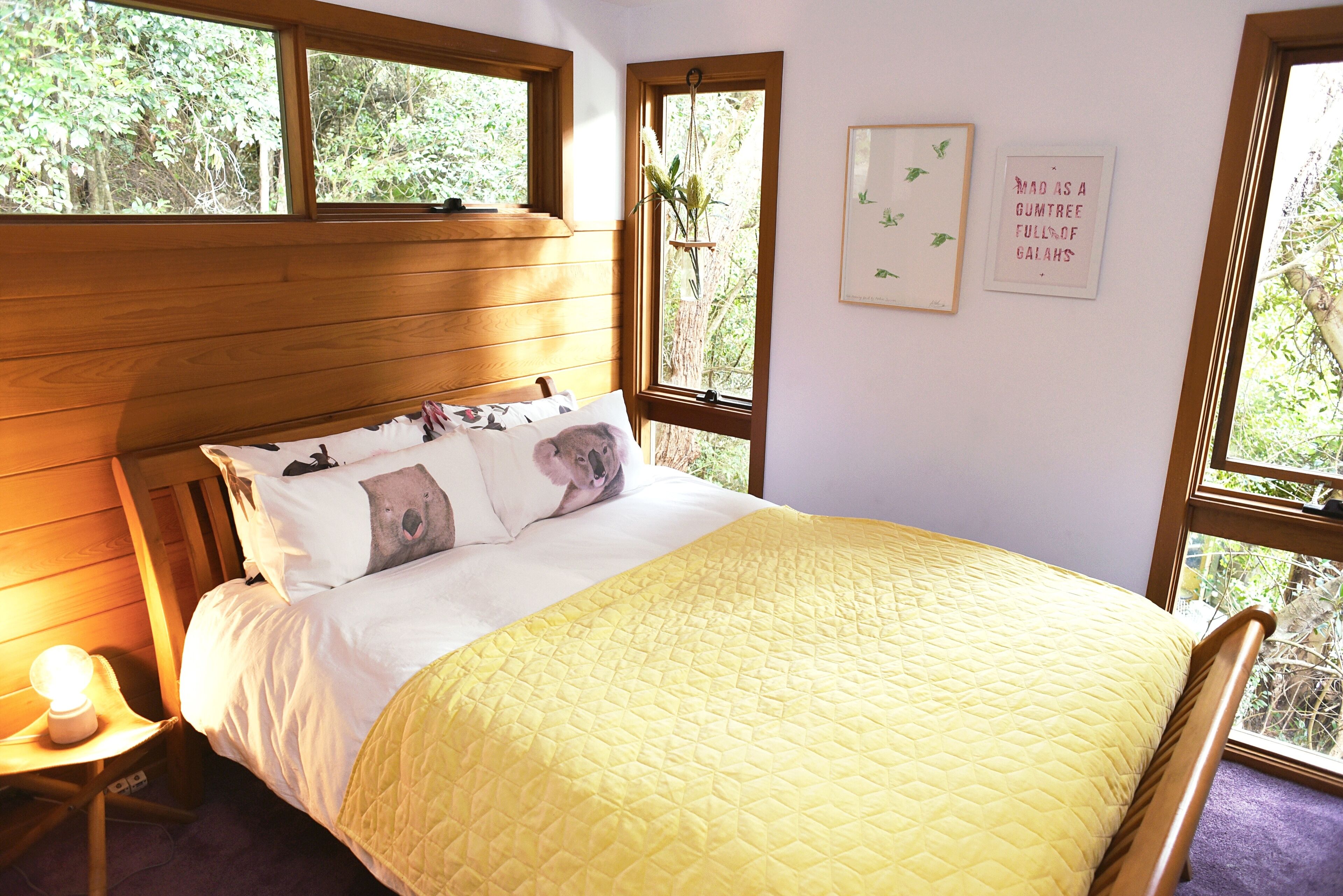 Une chambre à coucher avec une tête de lit en bois, une couvre-lit jaune matelassée et une table de chevet avec une lampe.