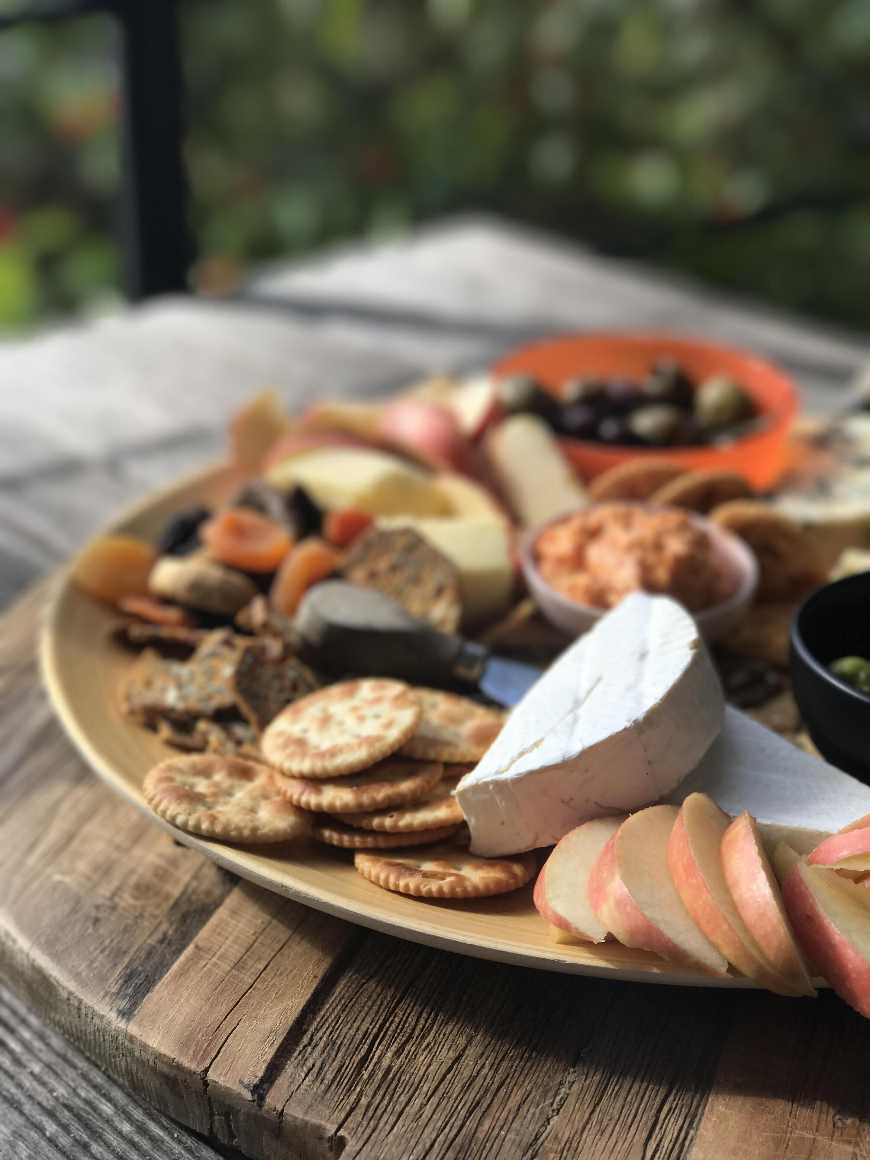 A wooden table with a cheese platter, crackers, and sliced apples.