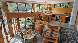 A spacious kitchen with large windows, a dining area with a high table, and a staircase with wooden steps.