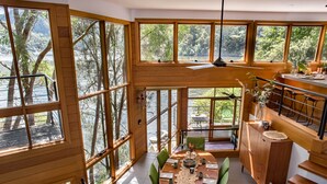 A dining area with a wooden table and chairs, large windows, and a view of the outdoors.