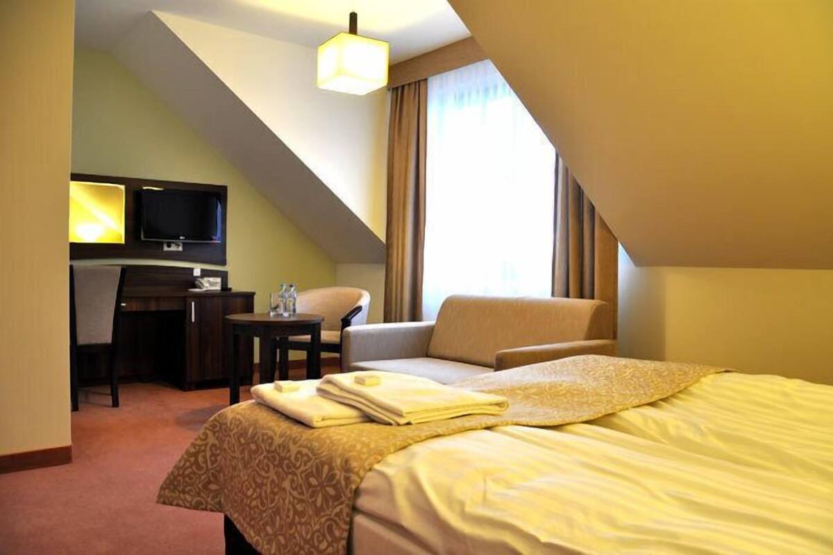A hotel room with a bed, a desk, a chair, a television, and a window with curtains.