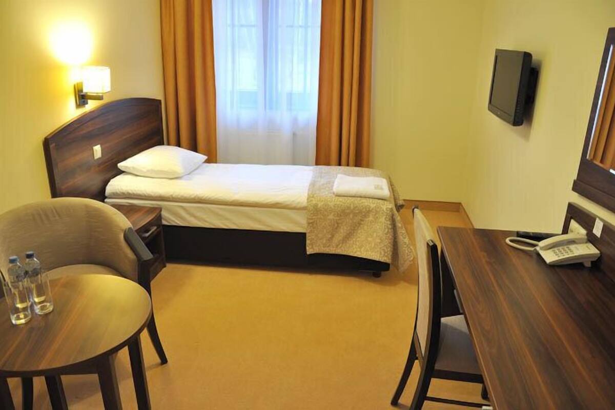 A hotel room with a bed, a desk, a chair, a TV, and a phone.