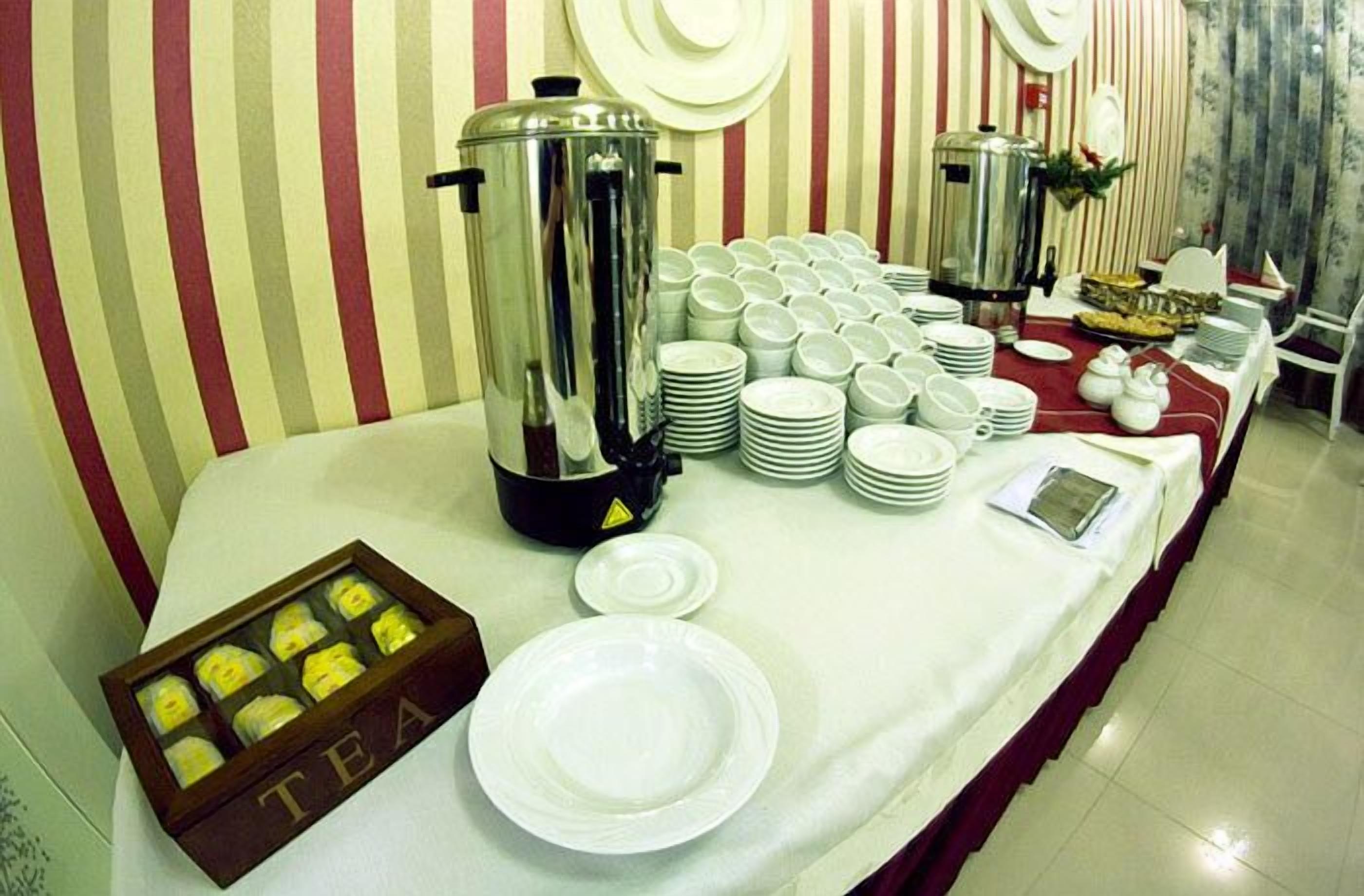 A buffet setup with multiple coffee pots, stacked plates, and a tea box.
