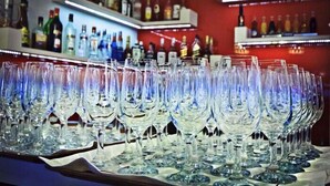 A bar area with multiple empty wine glasses arranged in rows on a tray, shelves with various bottles of liquor in the background. - Hotel Dudek (Mniów)