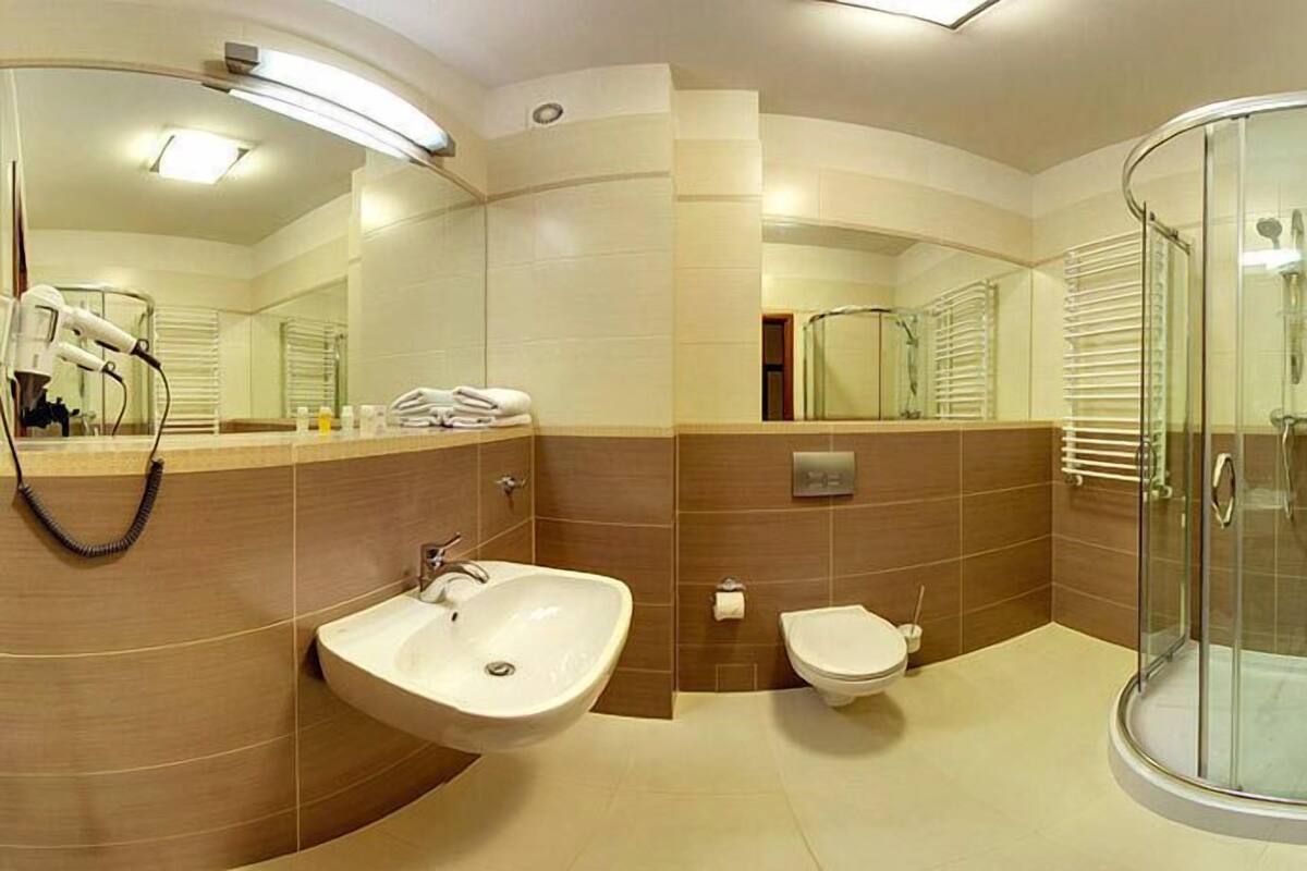 A modern bathroom with a curved sink, a toilet, a glass shower enclosure, and a large mirror.